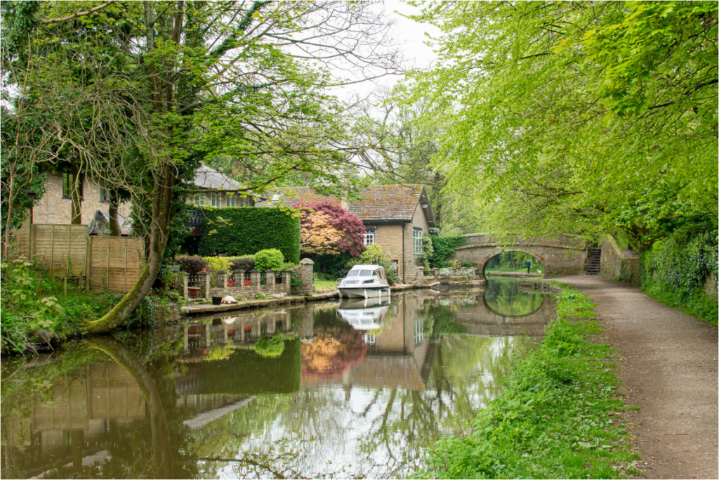 Macclesfield Canal with a bridge in the distance, houses on the left and a white moored boat outside one house.