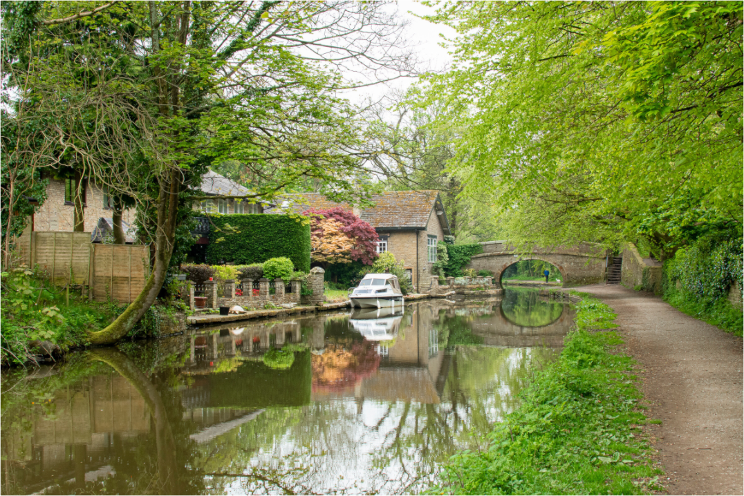 Macclesfield Canal with a bridge in the distance, houses on the left and a white moored boat outside one house.
