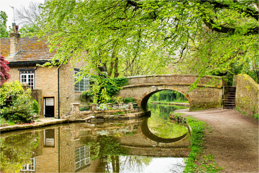 Bridge over the Macclesfield canal with beautiful reflections of the bridge and canal-side house. Overhanging trees are also reflected.