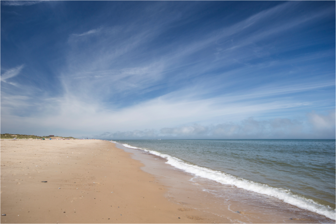 An empty sandy beach, gentle waves,   a blue sky and wispy cirrus clouds.