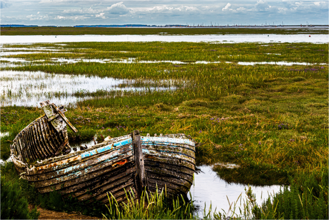 An old wooden boat, sitting on the grass in a waterlogged estuary. 